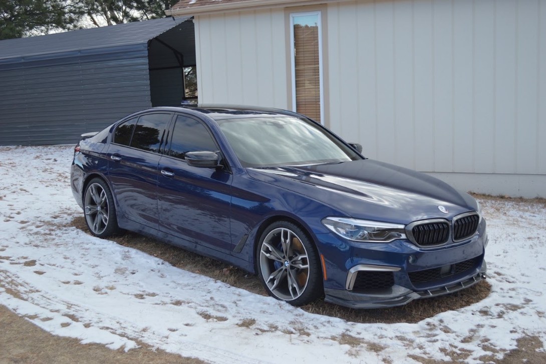 Blue BMW viewed from the front right with glossy paint beside a snowy driveway