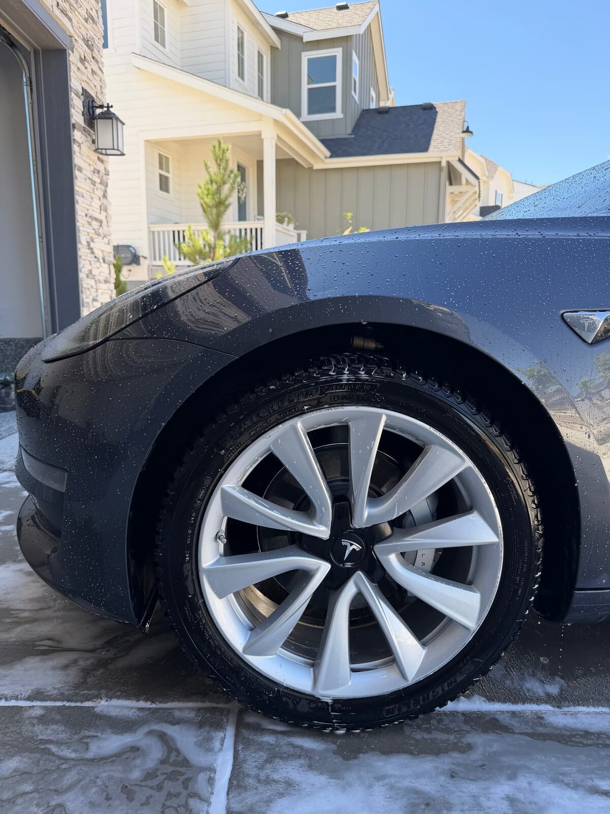 Gray Tesla Model 3 front wheel and tire freshly washed in a home driveway
